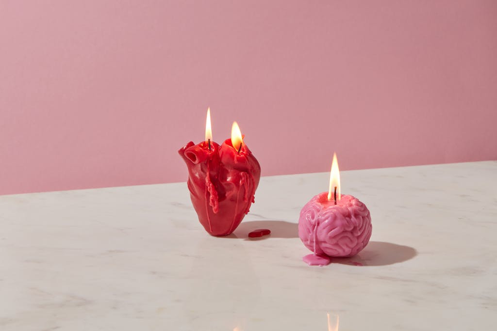 Heart and brain shaped candles lit on a marble surface against a pink background.