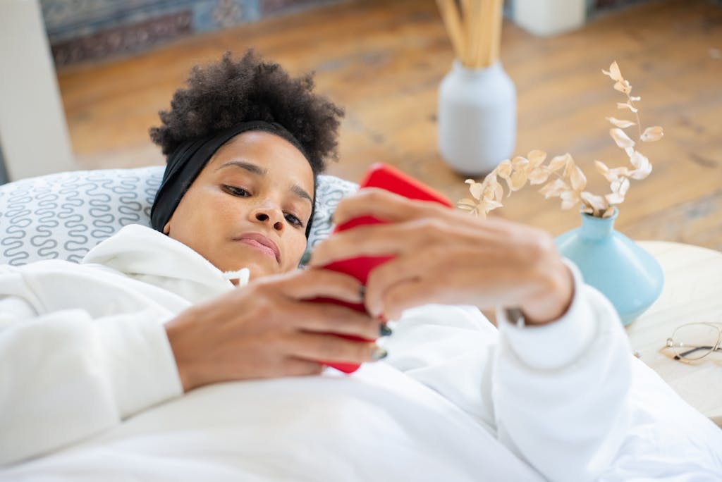 Woman lying on couch in white jacket using a smartphone, indoors setting.