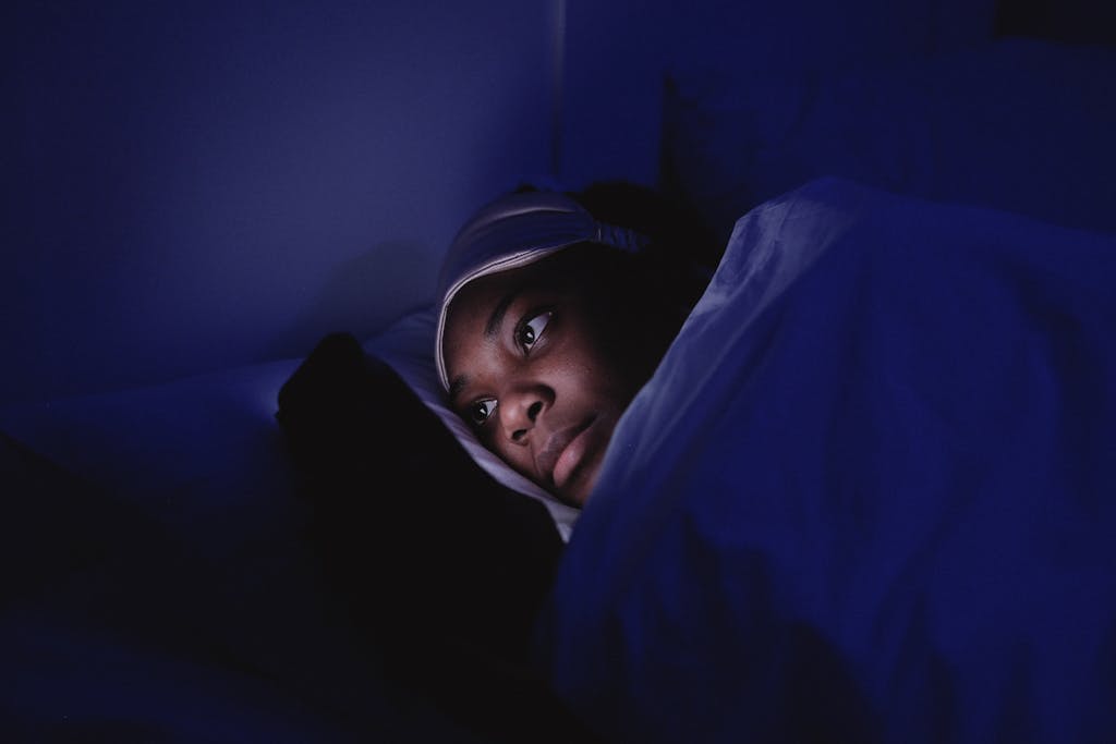 A woman lies in bed at night using her smartphone, illuminated by its screen.