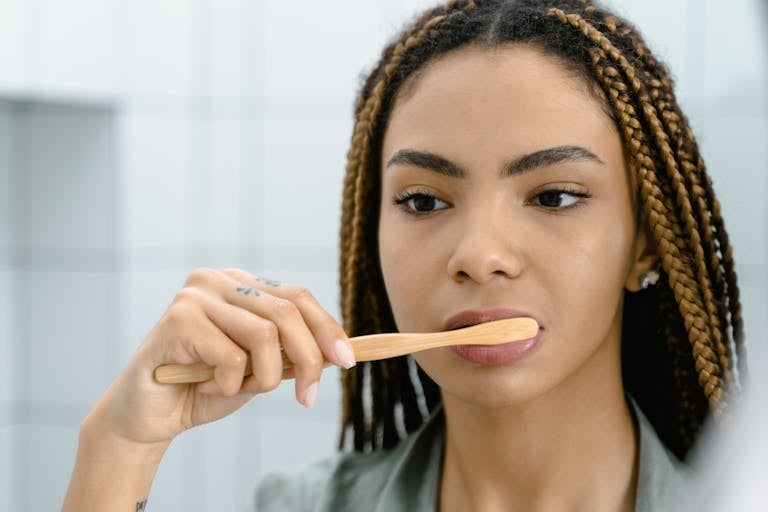 Close-up of a woman with braided hair brushing her teeth, highlighting oral hygiene.