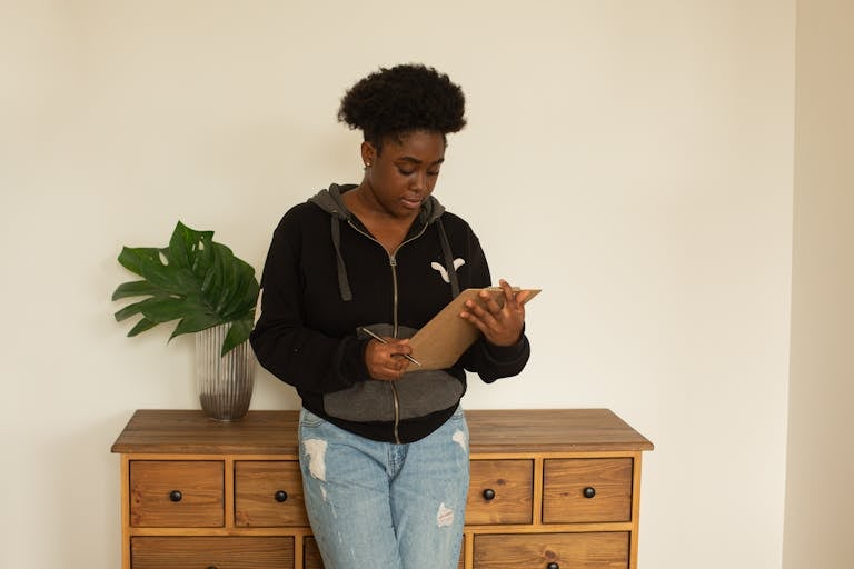 Woman with afro hair standing indoors reading a clipboard, showcasing focus and reflection.