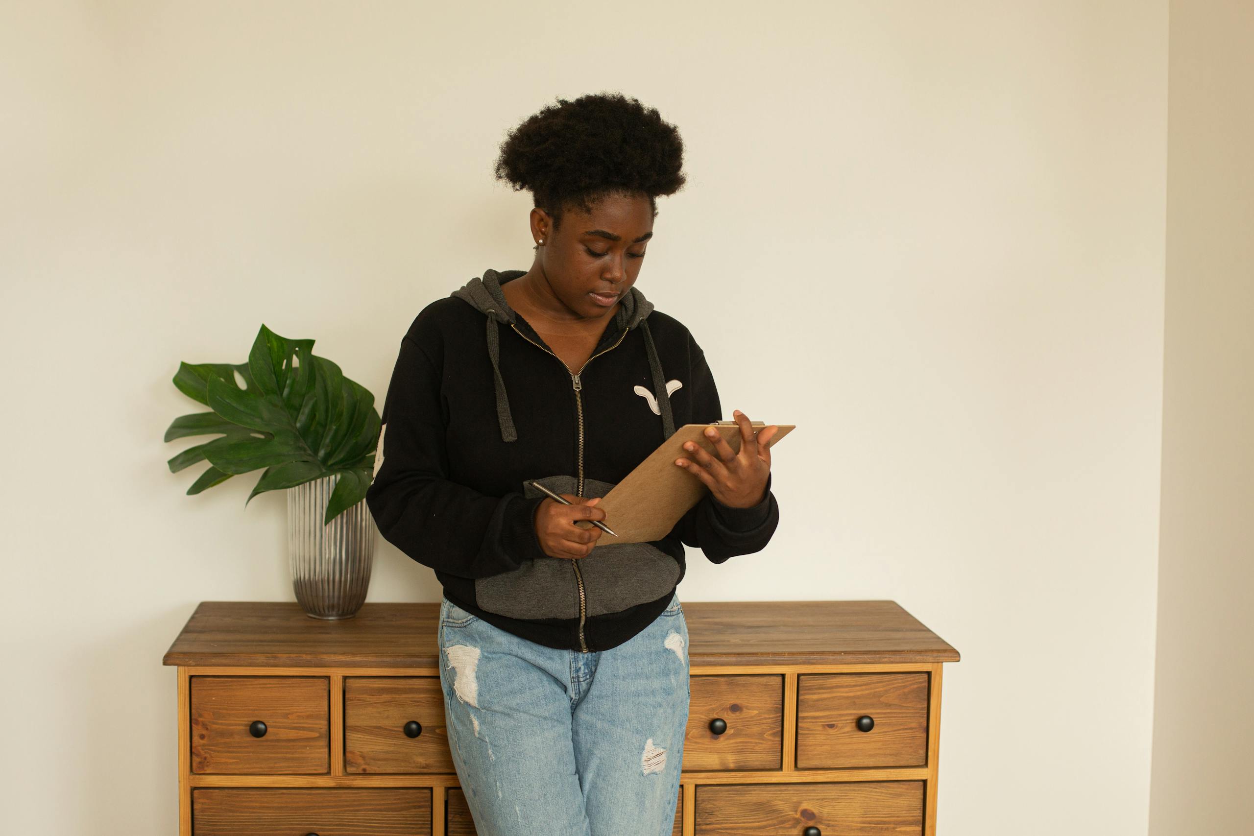 Woman with afro hair standing indoors reading a clipboard, showcasing focus and reflection.