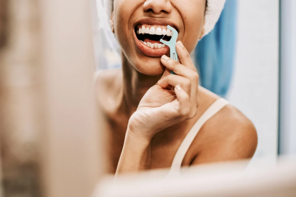 Woman using a floss pick in the bathroom mirror after brushing